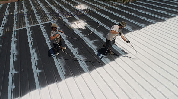 Roofers applying butyl elastomeric coating to a metal roof