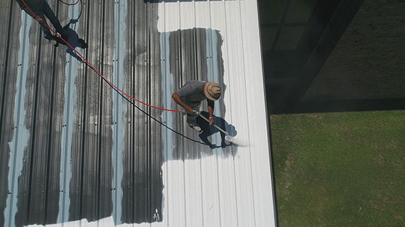 Roofers spraying butyl elastomeric coating on a commercial metal roof