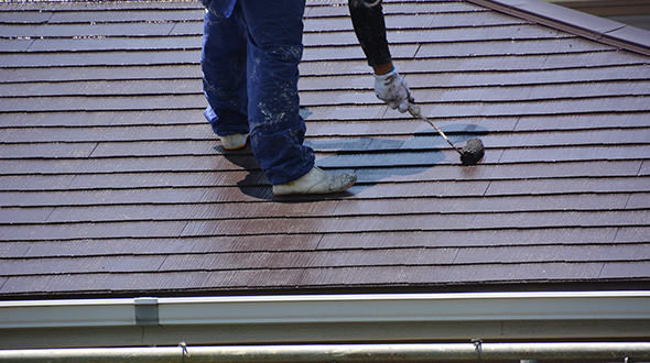 roofer applying acrylic latex paint on an asphalt shingle roof